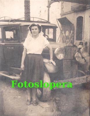 La Loperana Conchita Román junto a un taxi en la puerta de la Casa de Lopera en la Romería de Alharilla de Porcuna del año 1956.